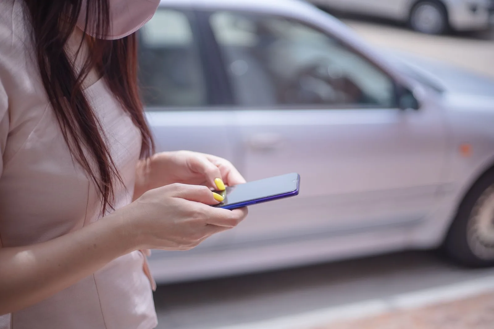 Woman checking her phone beside a parked car