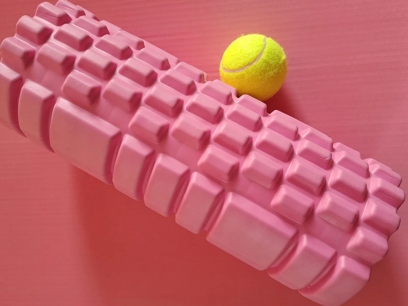 Pink foam roller and a tennis ball on a mat