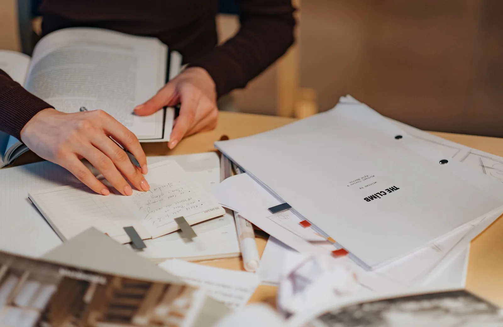 A person's hands writing notes by hand in an open notebook on a desk indoors.