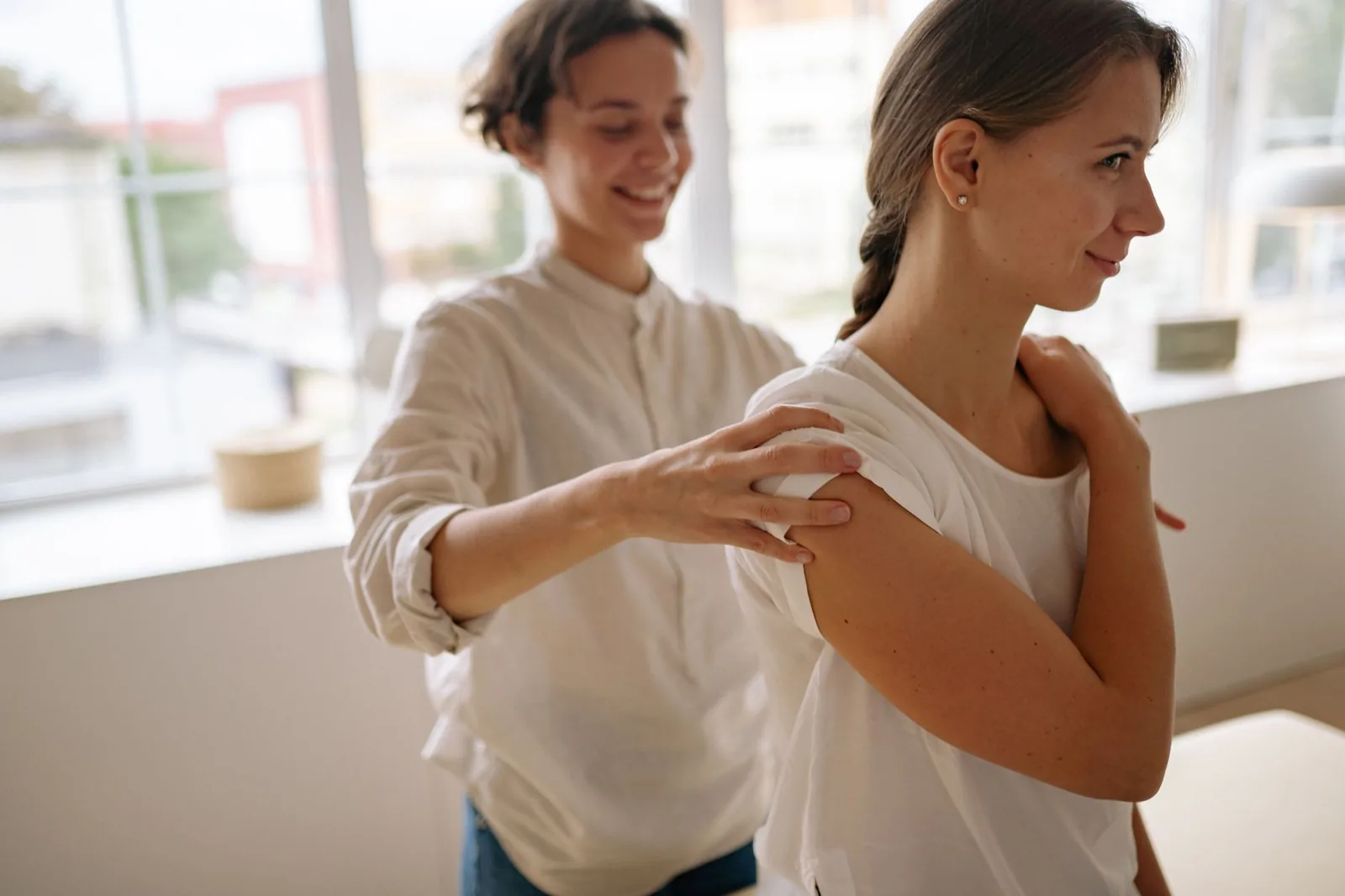 A woman receives a soothing shoulder massage in a sunlit room.