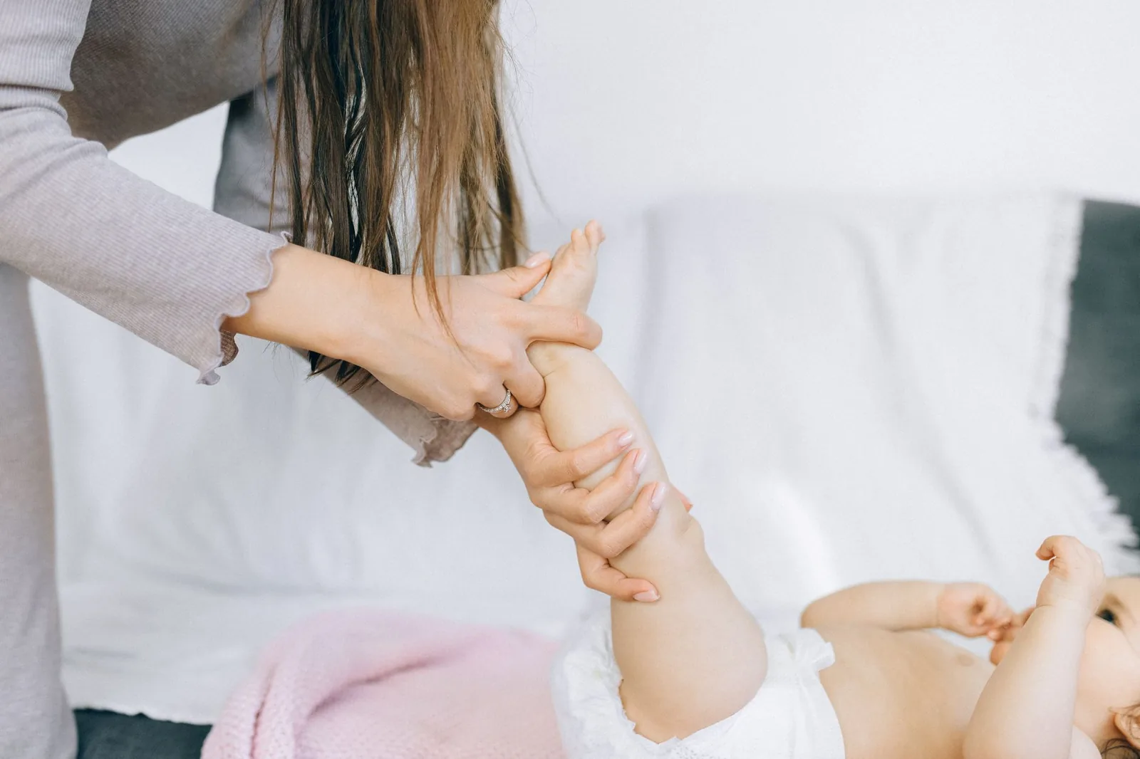 Mother massaging her baby's leg on a white blanket
