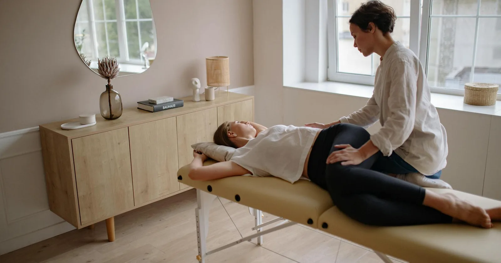 A therapist provides a calming massage to a client lying on a massage table in a serene, well-lit room.